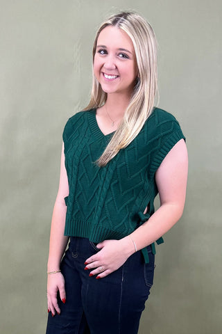 Woman wearing a green knitted vest against a plain background