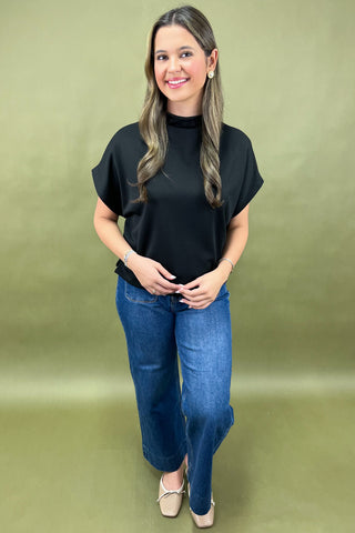 Woman wearing a black top and blue jeans against a green background