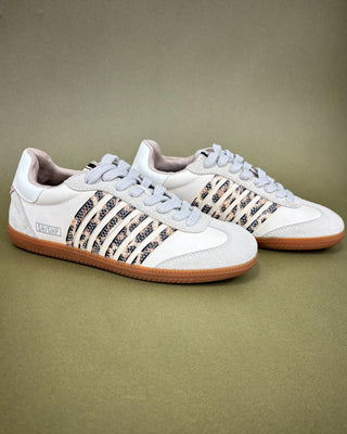 Pair of white sneakers with patterned accents on a beige background