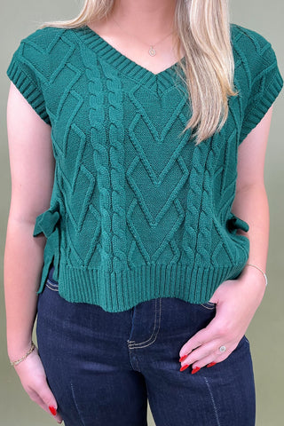 Person wearing a green knitted sleeveless sweater against a neutral background