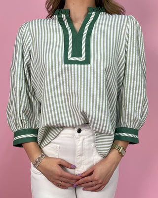 Green and white striped shirt with green trim worn by a person on a pink background