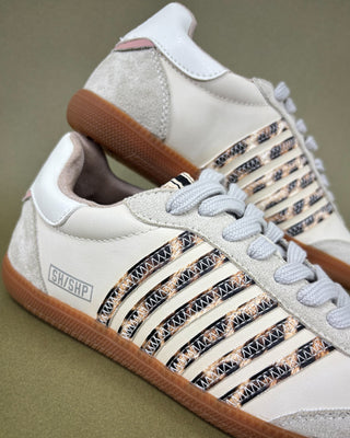 White sneakers with patterned side panels and brown soles on a beige background