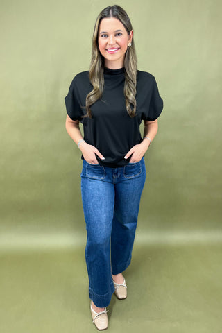 Woman wearing a black top and blue jeans against a green background