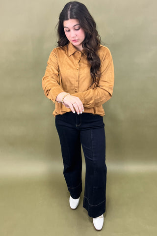 Woman wearing a mustard yellow shirt and black pants against a green background