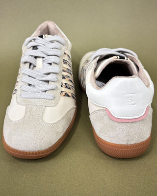 Pair of white sneakers with brown soles on a beige background
