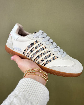 White sneaker with brown sole held by a hand against a green background