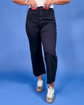 Black ankle-length straight leg jeans with a high-rise waist and raw hem, shown on model.