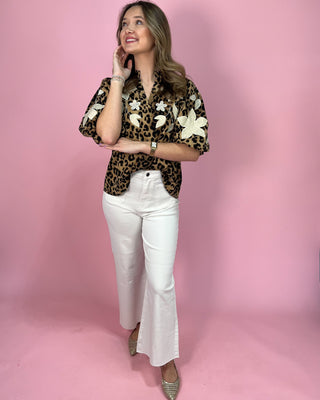 Woman wearing a leopard print top with white floral accents and white pants on a pink background