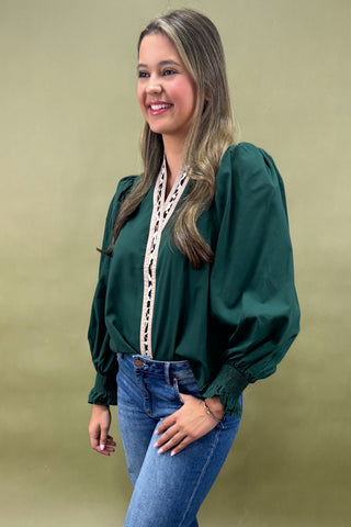 Woman wearing a green blouse with long sleeves and blue jeans against a beige background