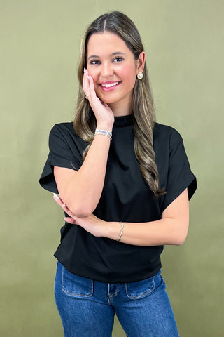 Woman wearing a black top and blue jeans against a green background