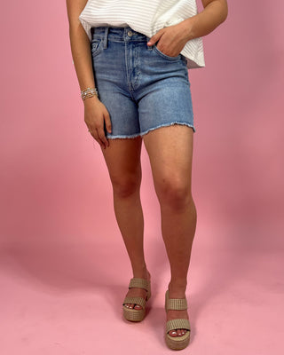 Person wearing denim shorts and a white top on a pink background