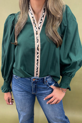 Green blouse with a decorative front panel worn by a person on a beige background
