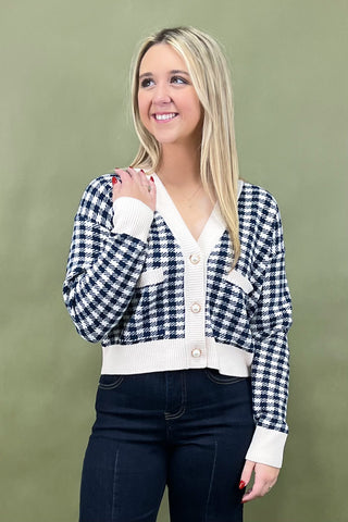 Woman wearing a checkered cardigan over a white shirt against a green background