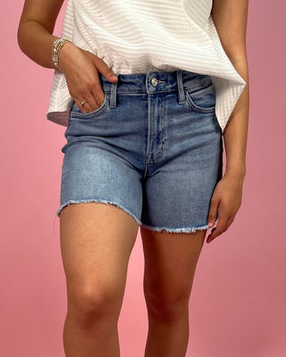 Person wearing blue denim shorts and a white top on a pink background