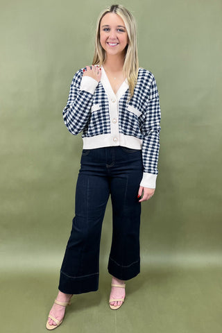 Woman wearing a checkered cardigan, white shirt, black pants, and pink shoes on a green background