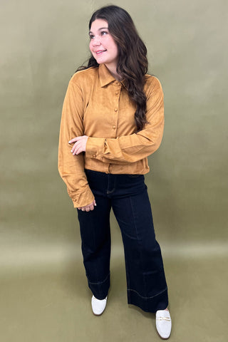 Woman wearing a mustard yellow jacket and dark blue jeans against a beige background