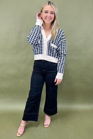 Woman wearing a checkered jacket, white shirt, dark jeans, and pink shoes on a green background