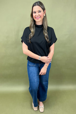 Woman wearing a black top and blue jeans against a green background