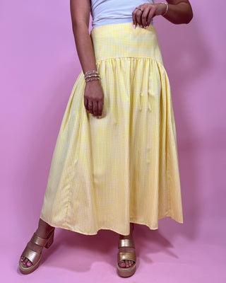 Person wearing a yellow checkered skirt on a pink background
