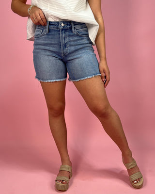 Person wearing blue denim shorts on a pink background