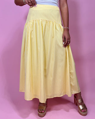 Person wearing a yellow checkered skirt on a pink background