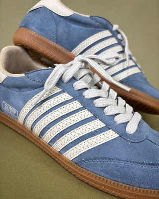Blue sneakers with white stripes and brown soles on a green background