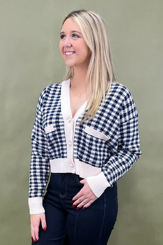 Woman wearing a black and white checkered cardigan over a white blouse against a plain background