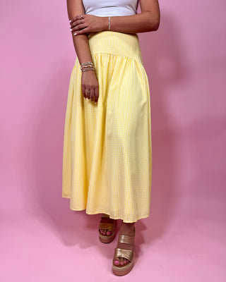 Person wearing a yellow checkered skirt on a pink background