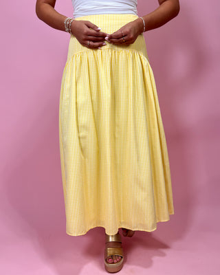 Person wearing a yellow checkered skirt on a pink background