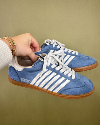Blue sneakers with white stripes held by a hand against a beige background