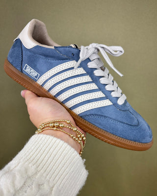 Blue sneaker with white stripes held by a person against a green background
