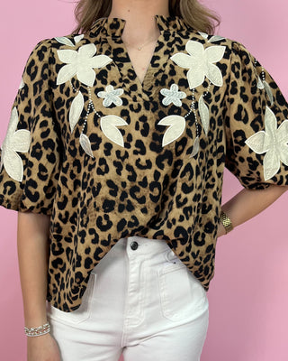Leopard print top with floral embellishments worn by a person on a pink background