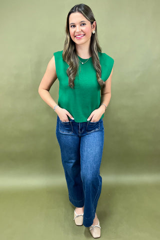 Woman wearing a green sleeveless top and blue jeans against a green background