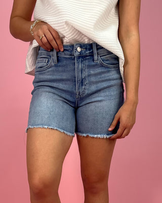Person wearing blue denim shorts on a pink background