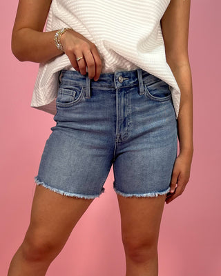 Person wearing blue denim shorts on a pink background
