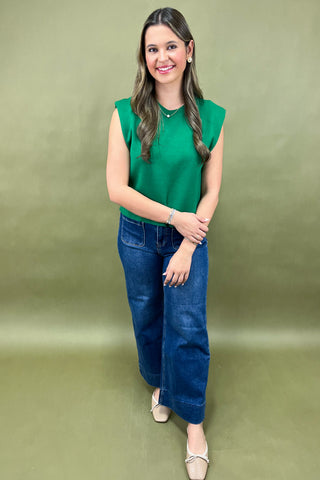 Woman wearing a green sleeveless top and blue jeans against a green background