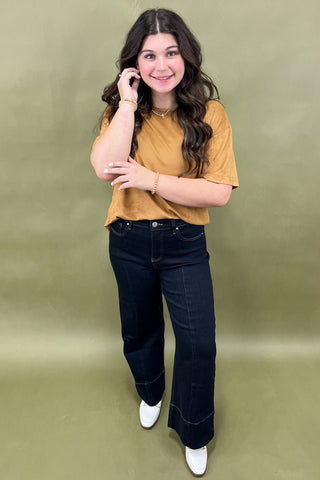 Woman wearing a mustard yellow shirt and dark blue jeans against a green background