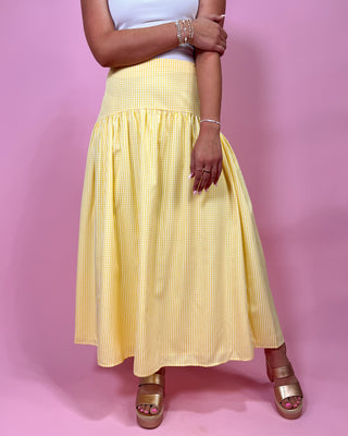 Person wearing a yellow checkered skirt on a pink background