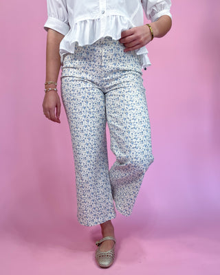 Person wearing white blouse and light floral pants on a pink background