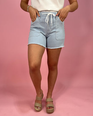 Person wearing light blue denim shorts on a pink background