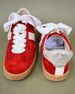 Red sneakers with white laces and a glittery sole on a green background