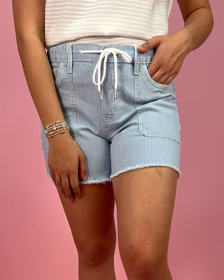 Person wearing light blue striped shorts with a white drawstring on a pink background