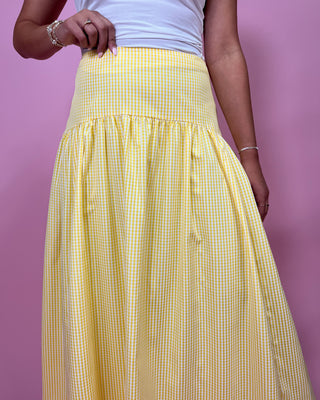 Person wearing a yellow checkered skirt against a pink background