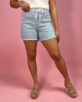 Person wearing light blue shorts on a pink background