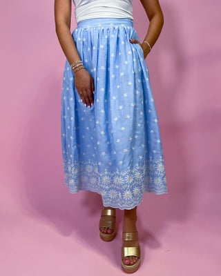Person wearing a light blue skirt with white floral patterns on a pink background