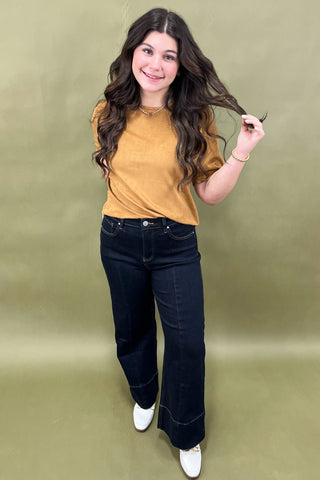 Woman wearing a mustard yellow top and dark blue jeans against a green background