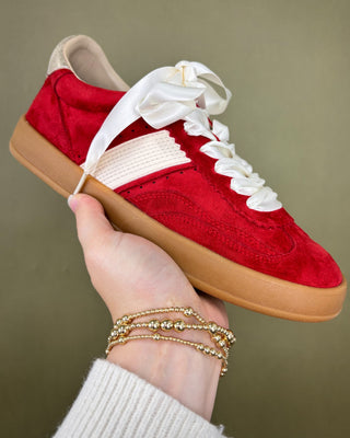 Red sneaker with white laces held by a hand against a green background