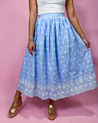 Person wearing a light blue floral skirt on a pink background