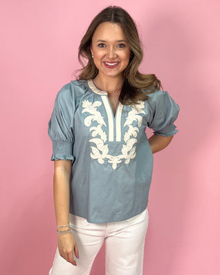 Woman wearing a blue blouse with white embroidery against a pink background