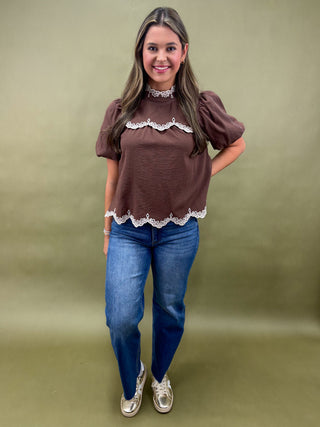 Woman wearing a brown blouse with lace details and blue jeans on a green background